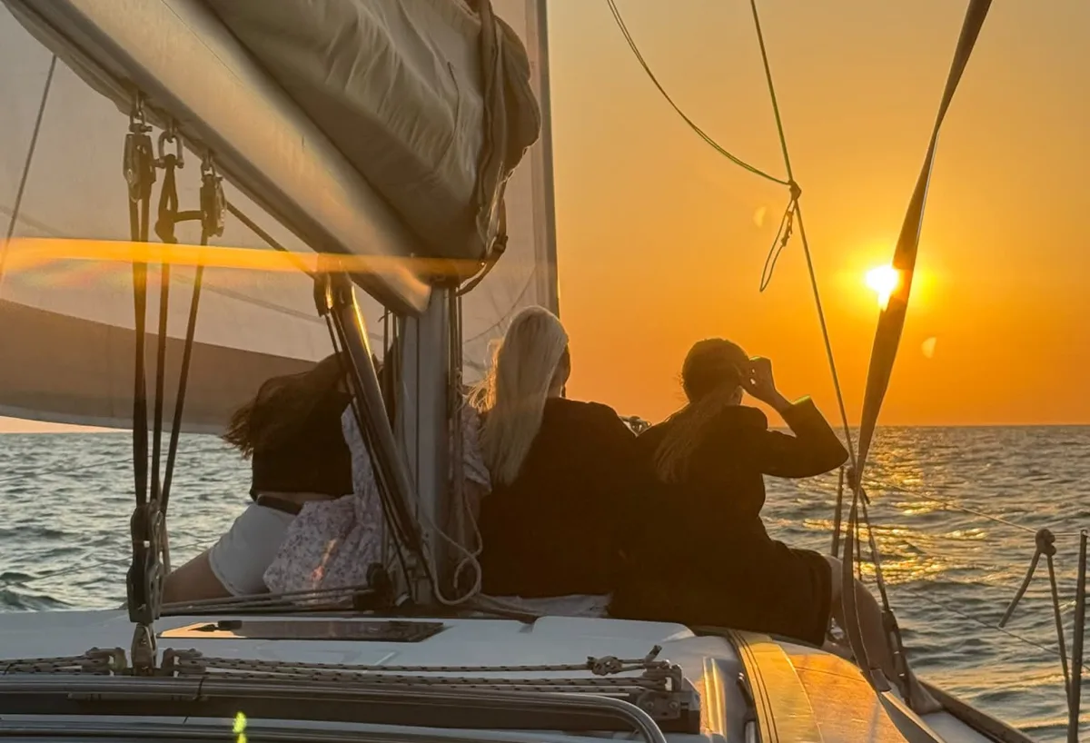Mediterranean sunset from a sail yacht deck in Herzliya Marina — three guests watching the horizon